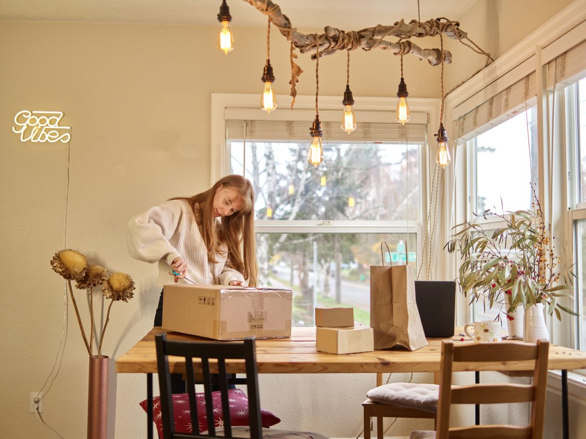A woman opening a parcel at a wooden table in a sunlit room
